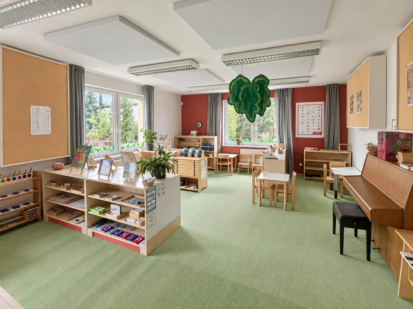 Montessori třída s nízkými poličkami s pomůckami, stolky a pianem.