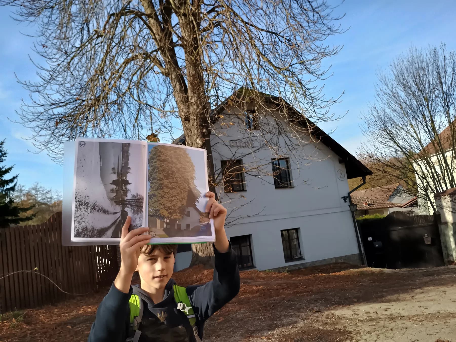 Chlapec drží knihu se starou fotografií před stavením v Kuří.