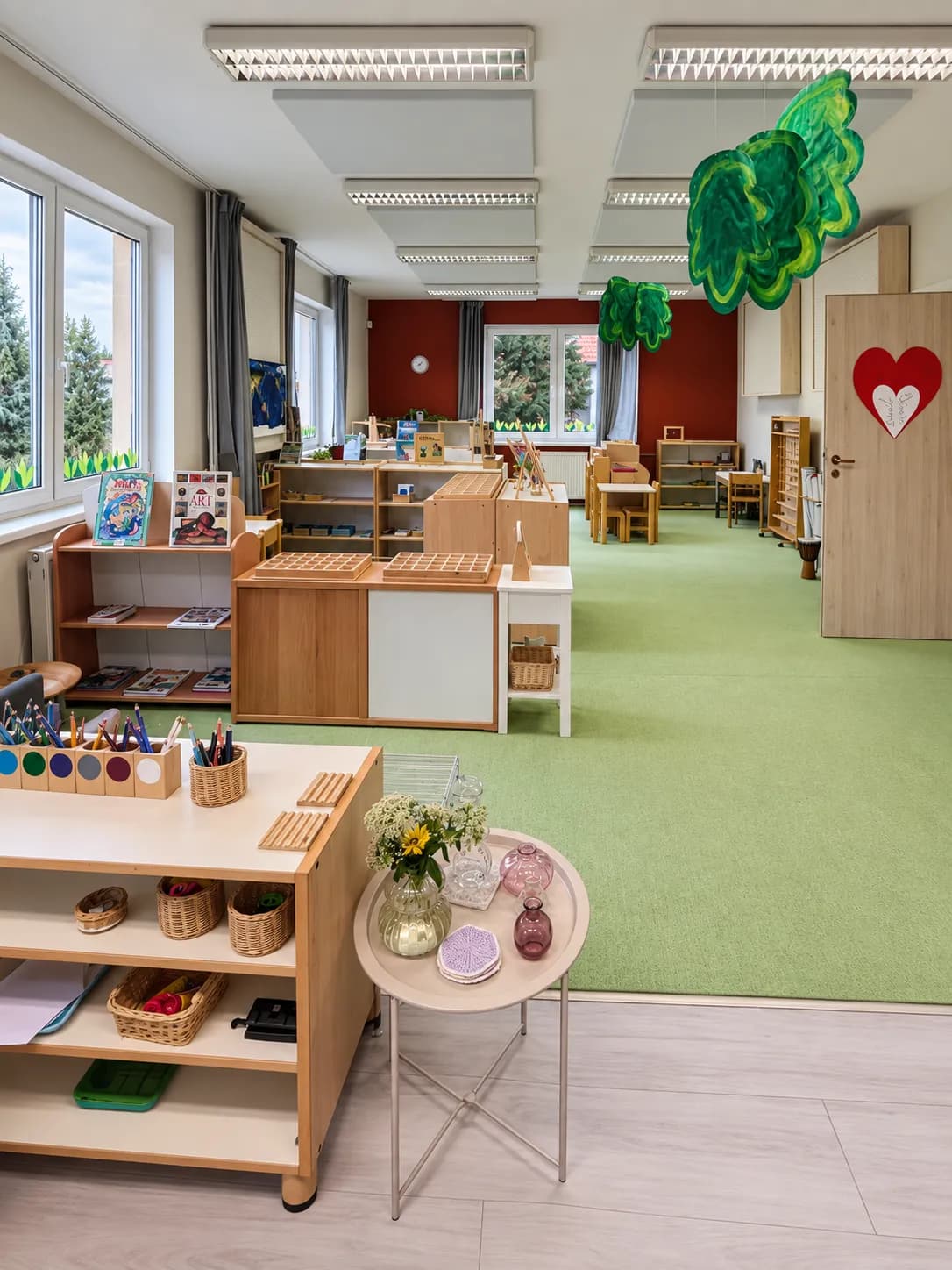 Montessori třída s poličkou s pomůckami a stolkem s květinami.