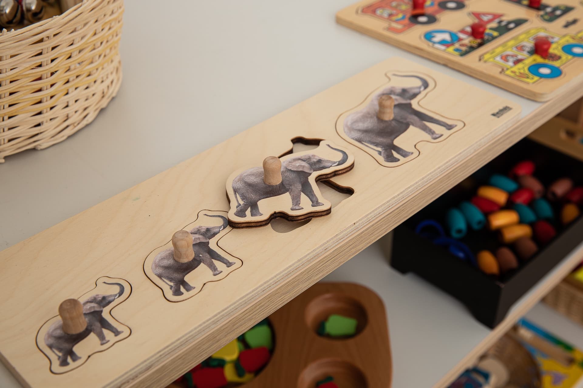 Dřevěné puzzle s rostoucími slony na polici s dalšími pomůckami.